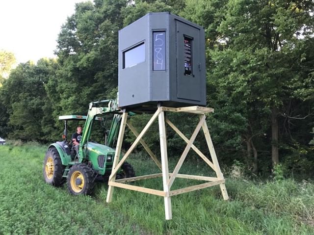 Tractor setting hunting blind on stand