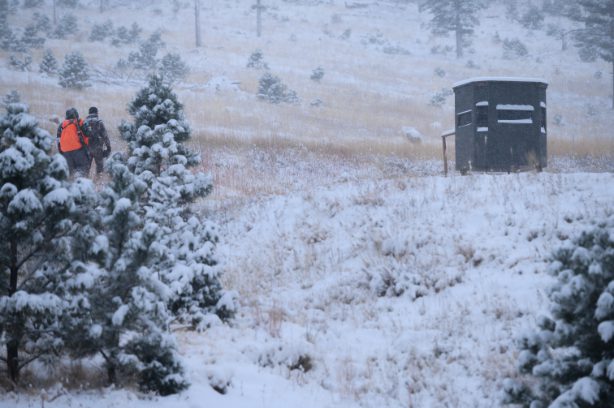 ambush hunting blind exterior in winter with 2 hunters walking towards it in snow