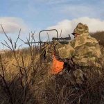 Hunter sitting in field aiming firearm